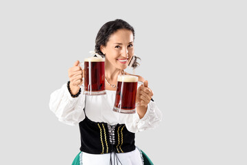 Beautiful mature happy Octoberfest waitress with mugs of beer on grey background