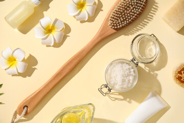 Composition with massage brush, natural body scrub and tropical flowers on color background