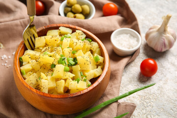 Wooden bowl of tasty potato salad with green onion and ingredients on grey background