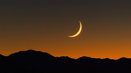 Crescent moon above silhouetted mountain range at sunset.