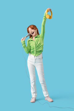 Fototapeta Teenage redhead girl with microphone and headphones singing karaoke on blue background