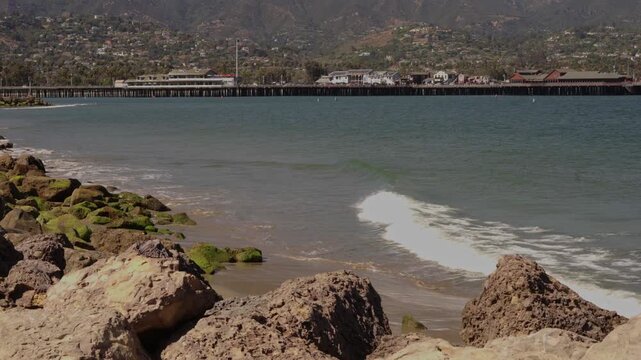 Rocky beach shoreline with moss covered stones and wooden pier in coastal town