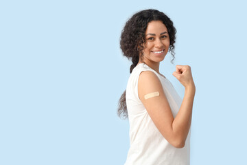 Young African-American woman with medical patch showing muscles after vaccination on blue background