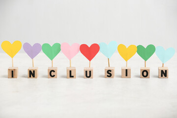 Cubes with word INCLUSION and colorful hearts on white table