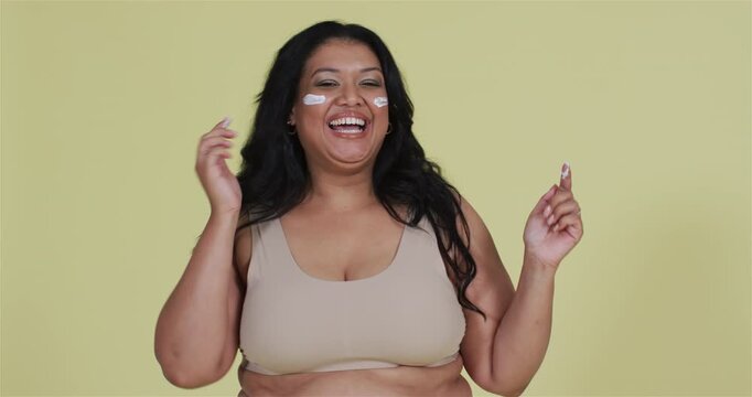 Laughing, tucking hair in studio, woman applying cream rubbing cheeks to hydrate skin, copy space