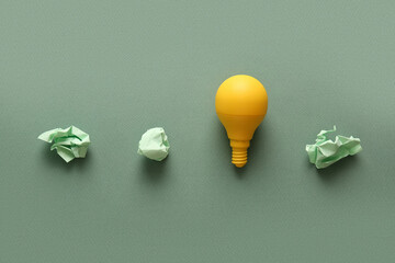 Yellow light bulb with crumpled paper on green background