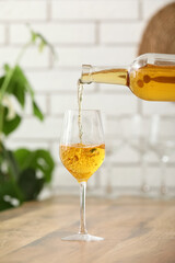 Pouring of white wine from bottle into glass on table in kitchen