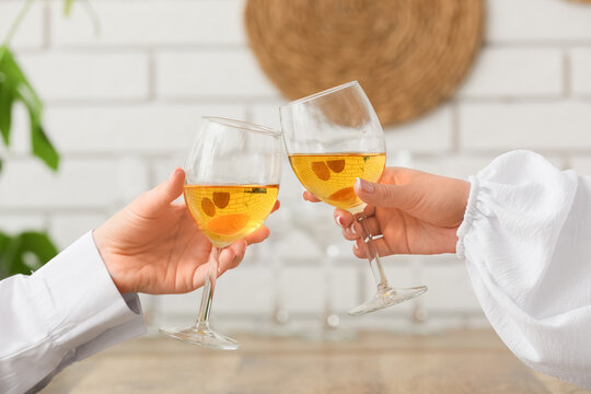 Female hands clinking glasses of white wine at table in kitchen