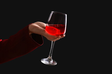 Female hand with glass of red wine on black background
