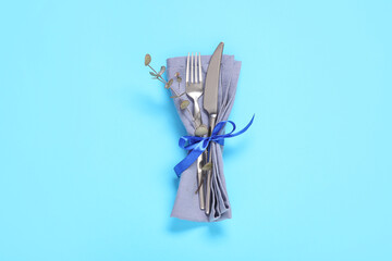 Napkin with cutlery, bow and eucalyptus on blue background