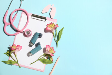 Clipboard with asthma inhalers, stethoscope and alstroemeria flowers on blue background
