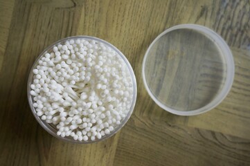 Container of cotton swabs on wooden surface with soft lighting and background objects