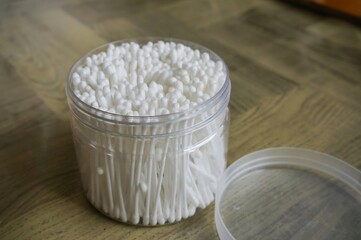 Container of cotton swabs on wooden surface with soft lighting and background objects