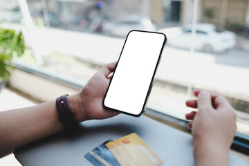 A person holding a smartphone with a blank white screen, with credit cards on the table nearby. A mockup for mobile banking or e-commerce apps.