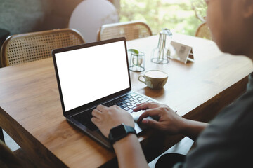 A person typing on a laptop with a blank white screen while working remotely in a bright and airy cafe. An ideal mockup for creative content.