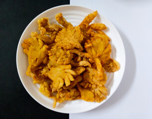 The view of fried Crispy Mushroom or Jamur Tiram Goreng Tepung Crispy, an Indonesian snack made from white oyster mushrooms dipped in seasoned savory flour. In white plate, in white background