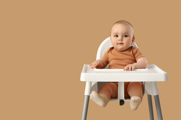 Cute little baby sitting in high chair against beige background