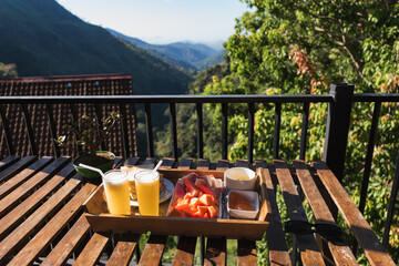 Wooden tray with fresh papaya, watermelon, juice and toasts served for breakfast on balcony with...