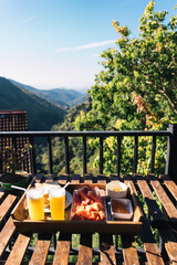 Fresh fruit, juice, and toast served on a wooden tray on a balcony overlooking a beautiful mountain range