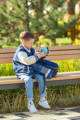 Smart happy school little boy with backpack sitting on bench in park, exploring a globe together, learning geography, dreaming on travel. High quality photo. Back to school concept