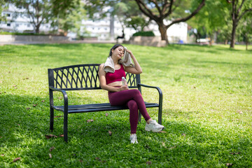 A woman is sitting on a park bench, wearing a pink shirt and red pants