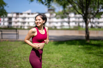 A woman is running in a park with a red tank top on