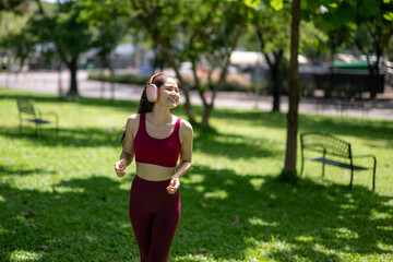 A woman in a red tank top and black leggings is running in a park
