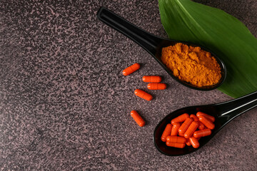 Spoons with turmeric root powder and capsules on dark grunge background