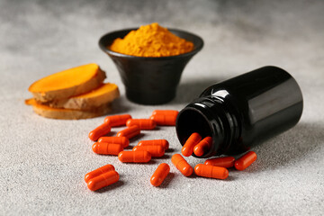 Bottle with capsules, turmeric root and bowl of powder on grey grunge background, closeup