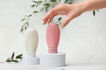 Plaster podiums with bottles of cream, female hand and eucalyptus on white grunge background