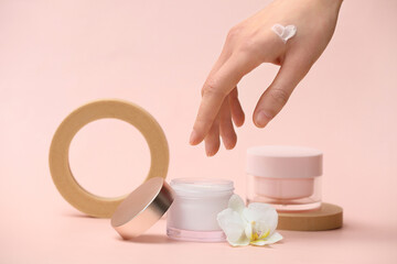 Female hand with plaster podiums, jars of cream and orchid flower on beige background