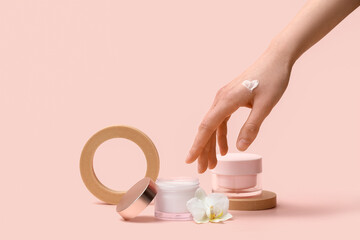 Female hand with plaster podiums, jars of cream and orchid flower on beige background