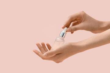 Female hands with bottle of serum on beige background