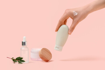 Female hand with bottle and jar of cream, serum and eucalyptus on beige background