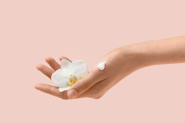 Female hand with cream smear and orchid flower on beige background