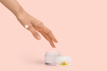 Female hand with jar of cream and orchid flower on beige background