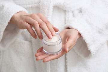 Young woman in bathrobe with jar of cream, closeup