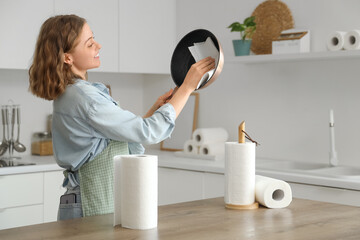 Young woman with rolls of paper towels cleaning frying pan near table in kitchen