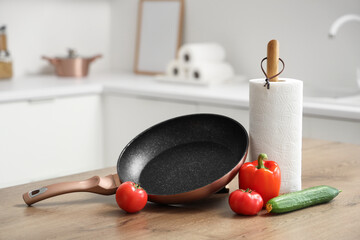 Roll of paper towels with frying pan and vegetables on table in kitchen