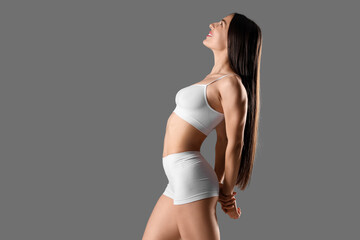 Happy young woman in stylish white underwear posing on grey background