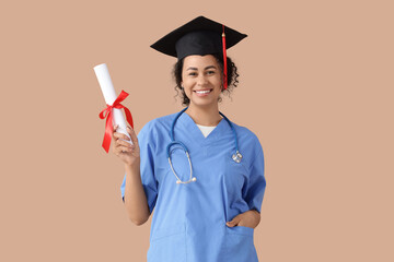 Female African-American medical student in graduation hat with diploma on beige background