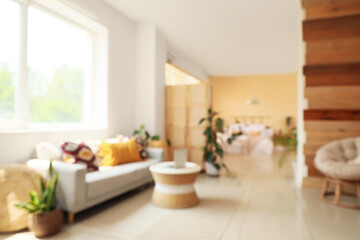 Blurred view of light room with sofa, table and modern laptop near window