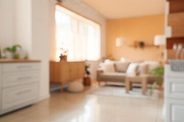 Blurred view of stylish room with beige sofa, table, chest of drawers and white counters