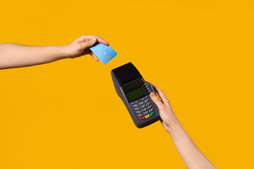 Hands with payment terminal and credit card on yellow background