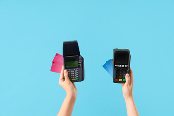 Hands holding payment terminals with credit cards on blue background