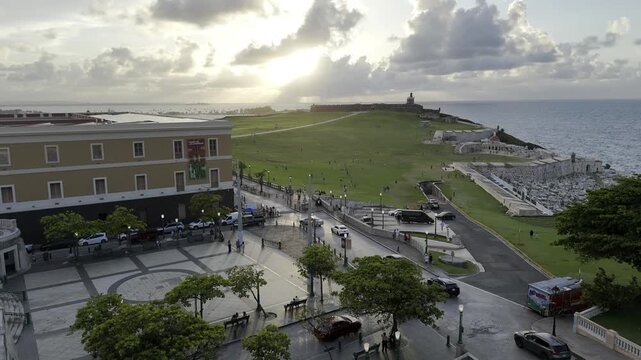 Drone rises up over Plaza del Quinto Centenario facing a sunset behind Castillo San Felipe del Morro in San Juan, Puerto Rico