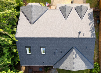 Brand new roof on a house in a residential neighborhood. The black shingles have been installed as a replacement on the older home for improvement. 