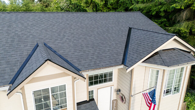 Brand new roof on a house in a residential neighborhood. The black shingles have been installed as a replacement on the older home for improvement. 