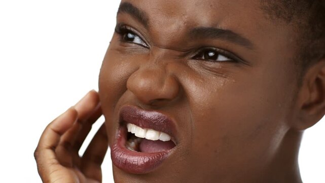 A young African American woman with short hair shows a pained expression while holding her face. She appears isolated against a neutral background, suffering from pain in teeth