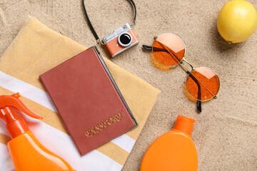 Passport with lemon and beach accessories on sand, top view